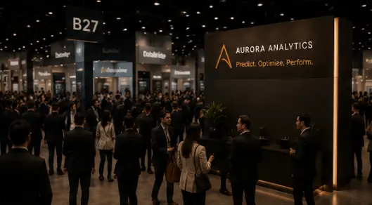 A branded exhibition booth reading “Aurora Analytics: Predict. Optimize. Perform.” with a few people standing near it on a crowded show floor.