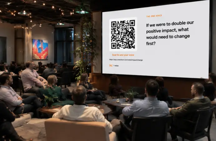 People seated around low tables at an evening venue, watching a One Voicer screen that asks “If we were to double our positive impact, what would need to change first?”