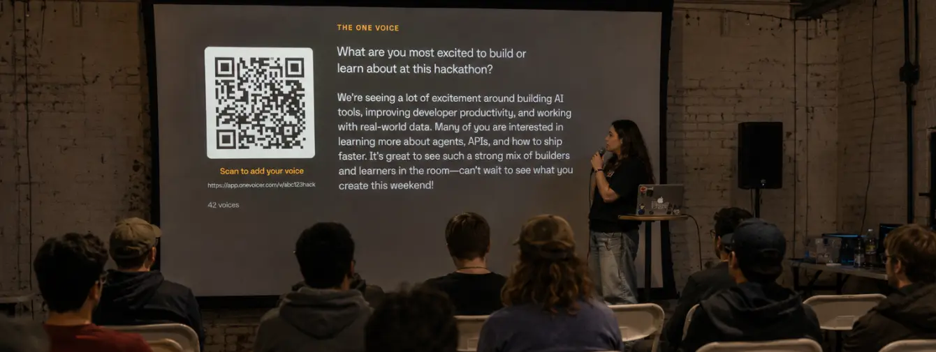 An organizer with a microphone on stage in front of a large screen showing the question “What are you most excited to build or learn about at this hackathon?”, a QR code labelled “Scan to add your voice,” and a blended answer from 42 voices.
