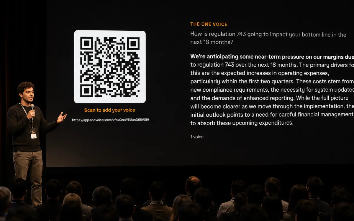 A conference speaker on stage beside a slide showing a QR code that reads “Scan to add your voice.”